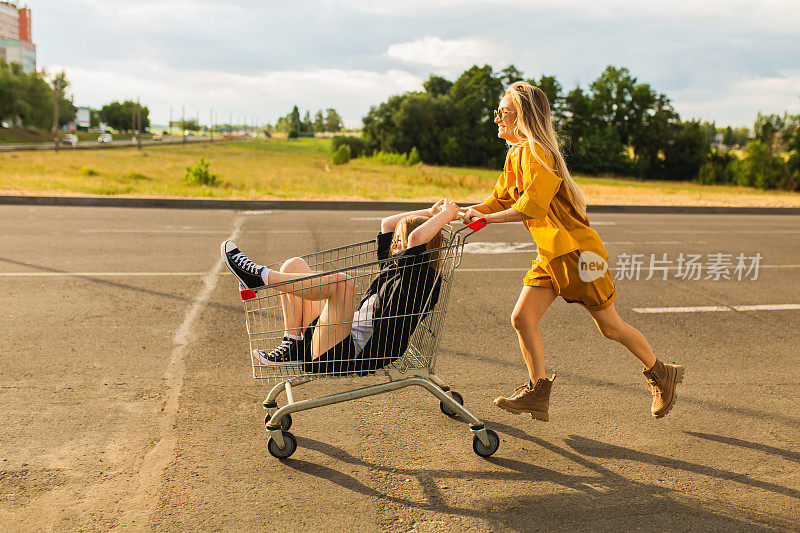 两个年轻的金发女孩在购物车里玩得很开心。时尚的女人