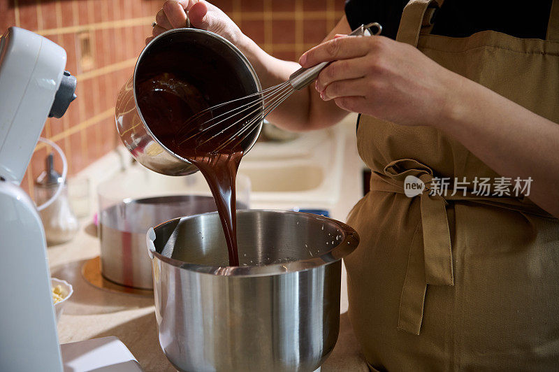 特写糕点师将融化的巧克力倒入行星搅拌器中，与奶油或打发的蛋白混合