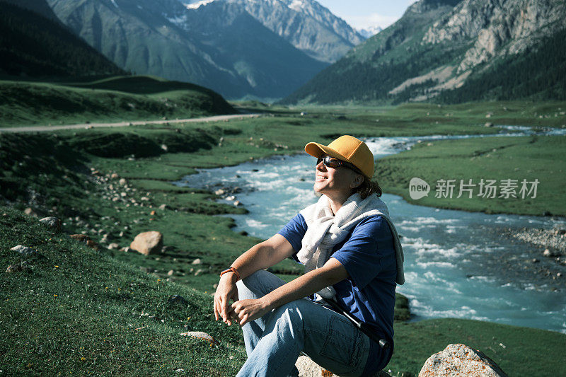 成熟的女游客在美丽的天山峡谷的山河边休息的肖像