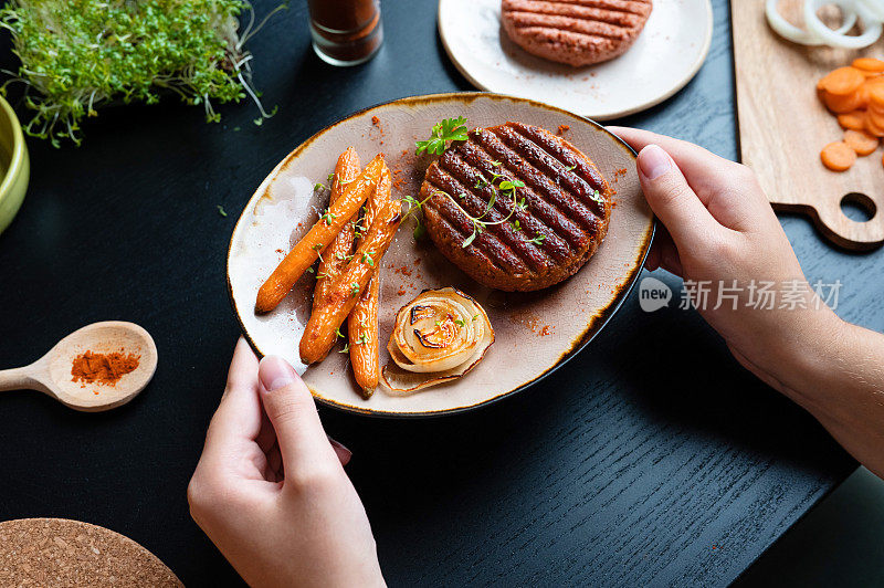 女性的手把一盘烤植物肉汉堡放在桌子上。