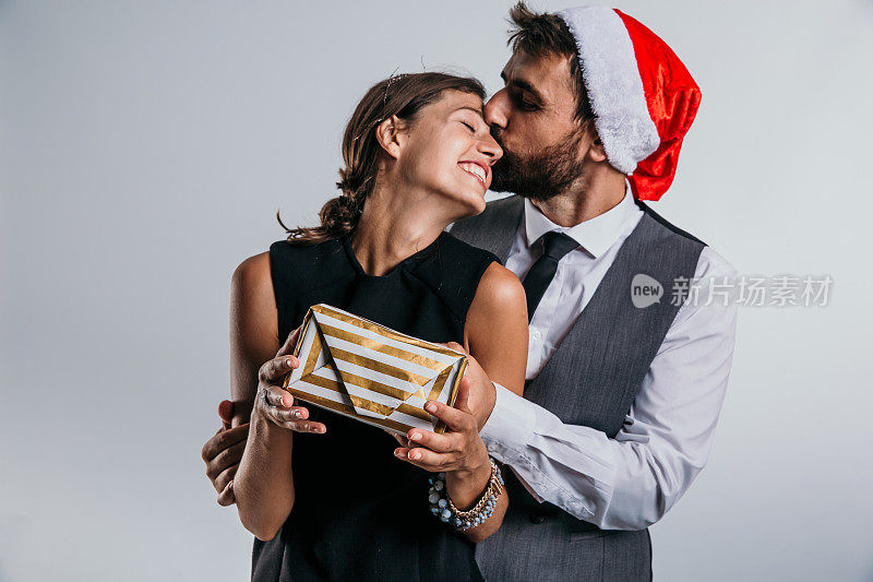 一对商业头脑敏锐的夫妇在工作室里戴上圣诞老人的帽子，拿着包装精美的礼物，沉浸在新年的喜悦中。