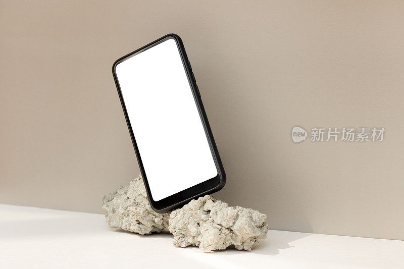 原型模板智能手机平衡在米色背景上的天然石材。手机与空白屏幕模板