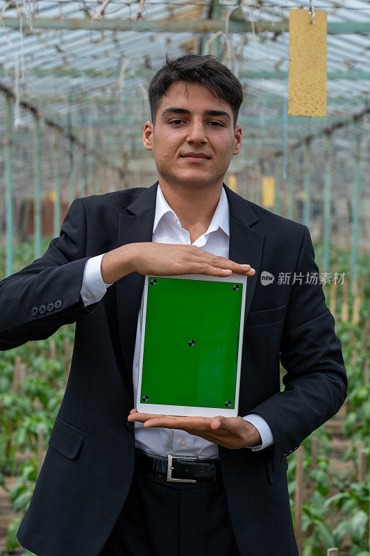 年轻的企业家用他的数码平板电脑控制着温室