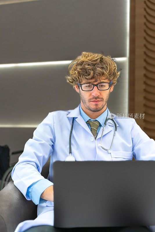 休息时间的效率:年轻的白人医生在走廊休息时花了一点时间在笔记本电脑上工作