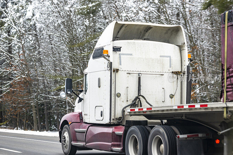 长轮大钻机双色半挂车运输有盖货物的平板半挂车在冬季有雪的道路上行驶