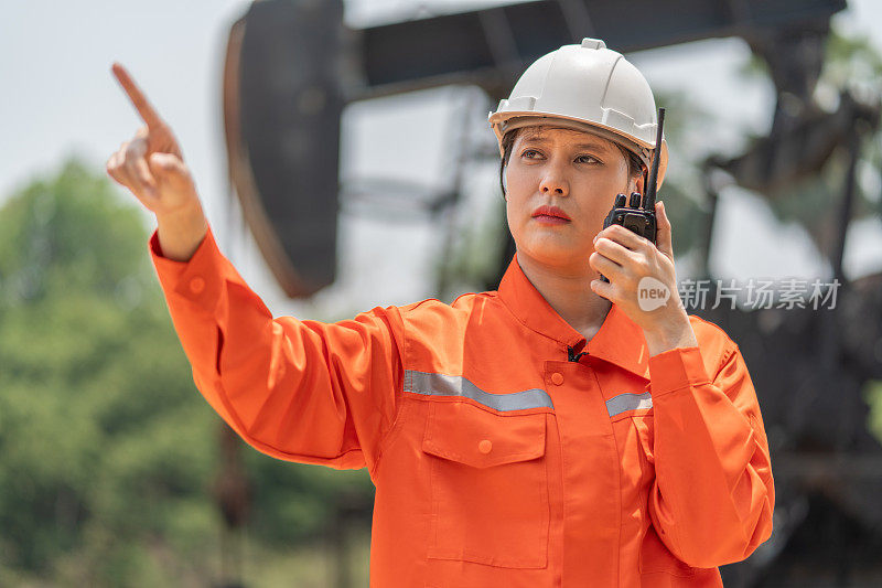 一名身穿橙色工程师连身衣、头戴白色安全帽的女工程师，手拿对讲机，站在一名石油钻探工面前