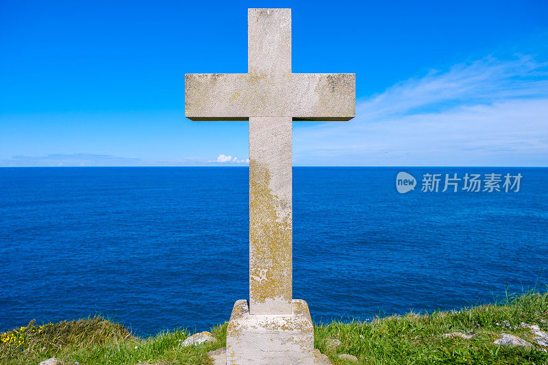 一个基督教十字架高高矗立在一座小山上，在浩瀚的大海的背景下投下阴影，海浪在下面撞击。这场面散发着庄严肃穆的气氛。