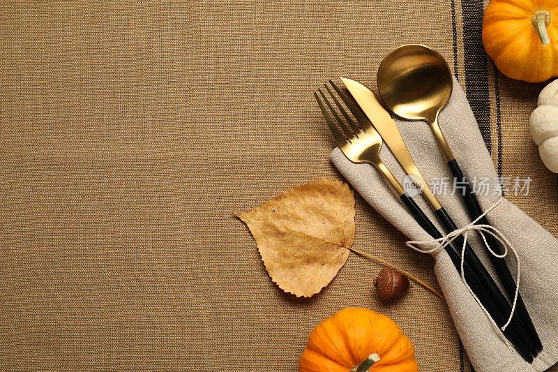 棕色桌布上的餐具、餐巾和南瓜，平摊着，留出文字的空间。表设置
