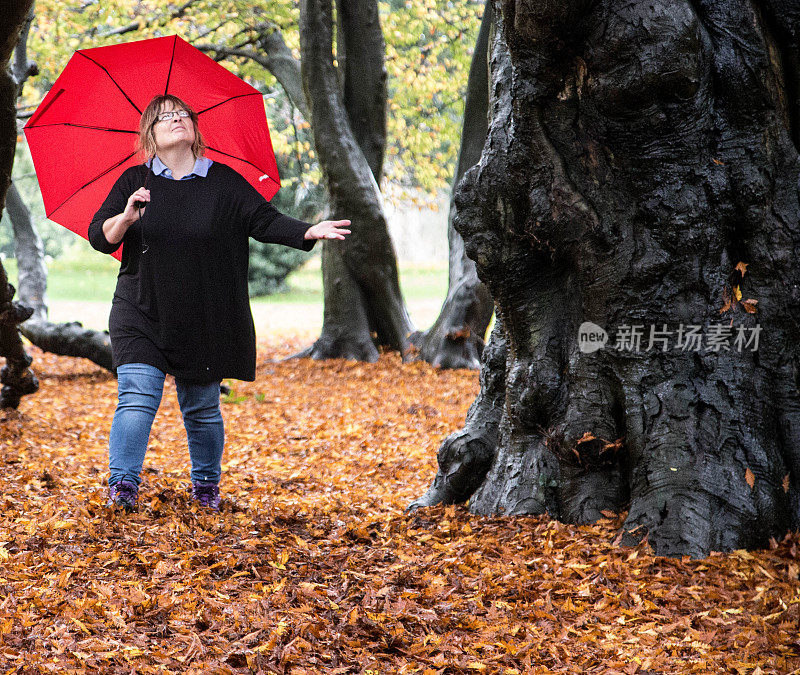 女人撑着红伞走过秋叶