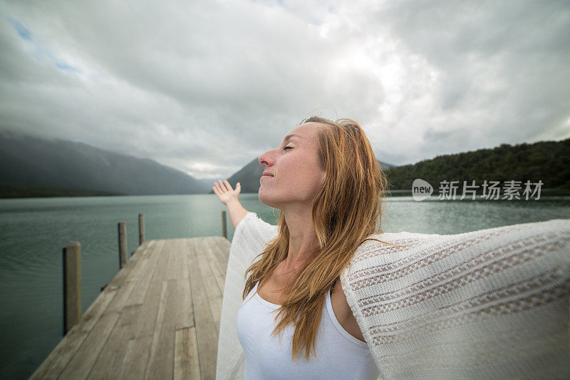 一个年轻女子的肖像在湖码头上张开双臂