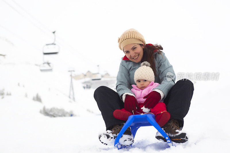 母亲和蹒跚学步的女儿享受雪橇