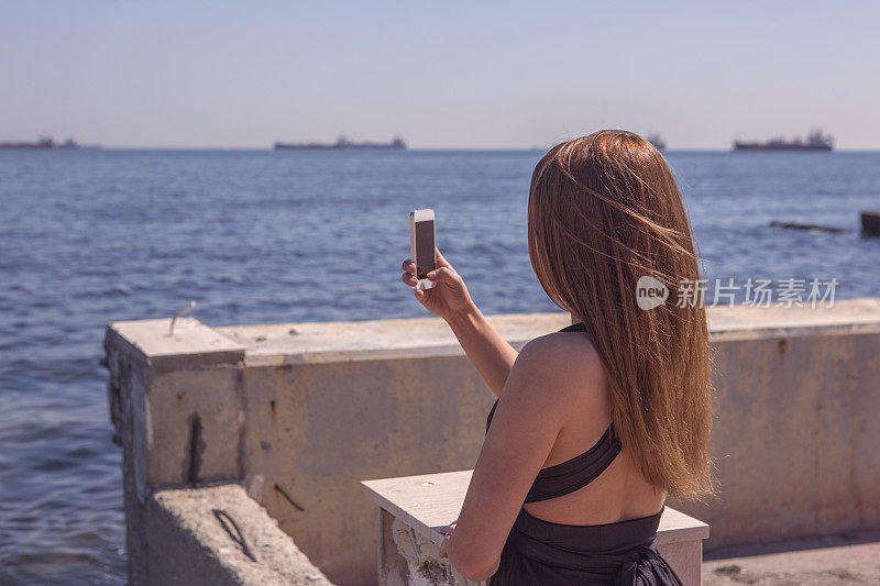 一名年轻女性在土耳其伊斯坦布尔马尔马拉海岸用智能手机拍照