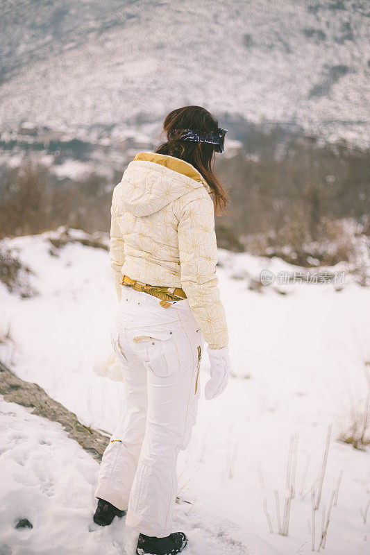 近景美丽的年轻女子在冬天的衣服站在一边，手拿木棍的背景雪山