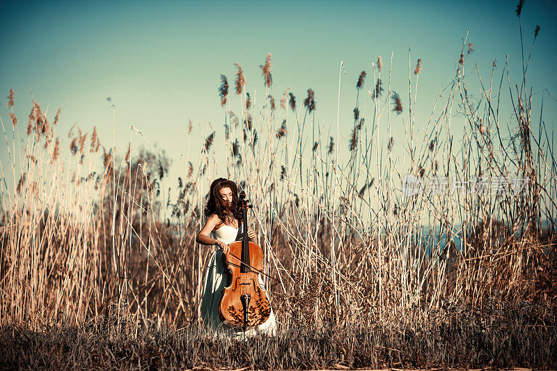 高高的草丛中拿着大提琴的女孩