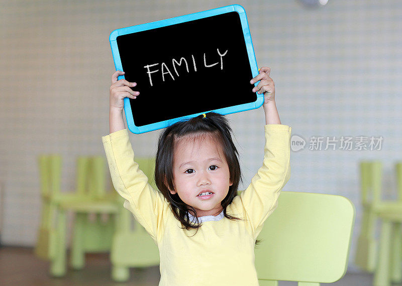 可爱的小女孩拿着写有“家庭”的黑板在儿童房。教育的概念。