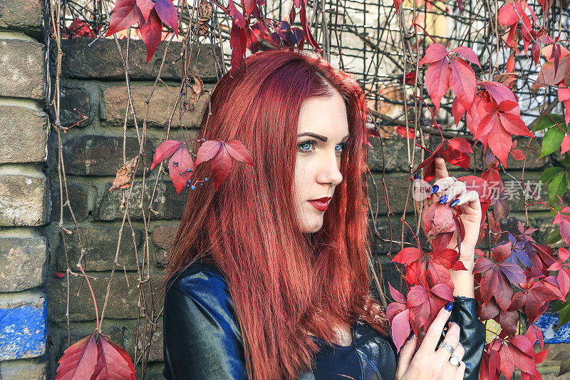 一个悲伤而忧郁的美丽的红头发女人的特写在多彩的秋叶中