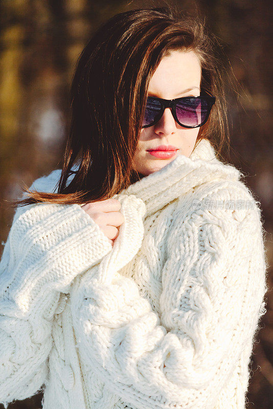 漂亮的年轻时尚的女人摆姿势，在一个阳光明媚的冬天，在公园里走时尚外套