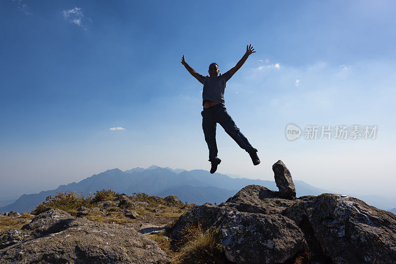 在山顶上举起手臂跳跃的男人