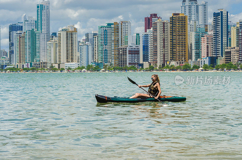 年轻女子在巴西海滩上划着皮艇漫步。