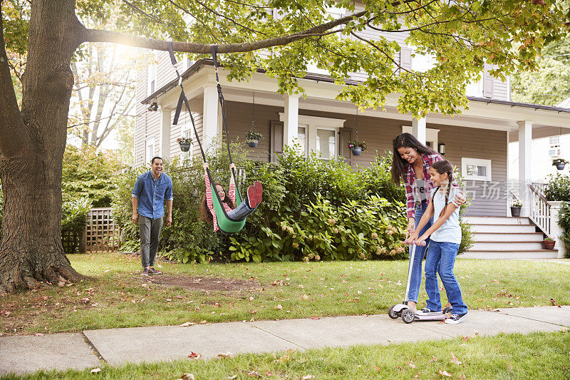 孩子们在房子外面玩花园秋千和滑板车
