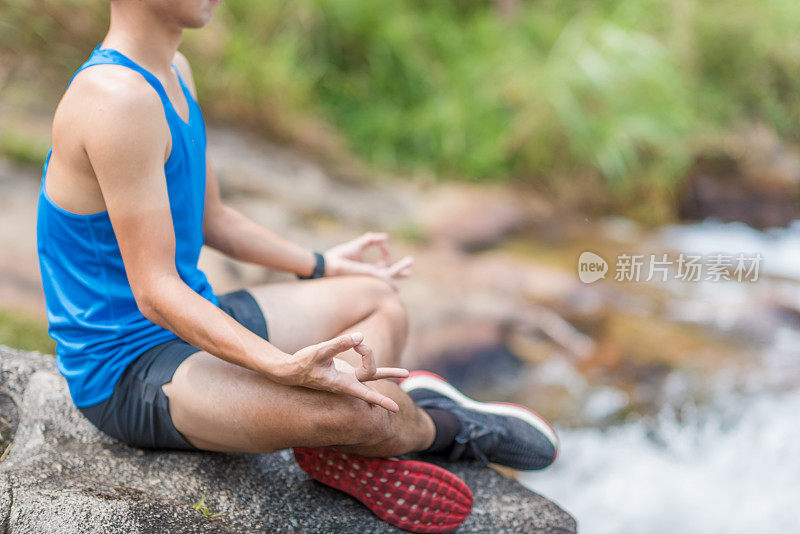 一个年轻的亚洲男人在瀑布做瑜伽