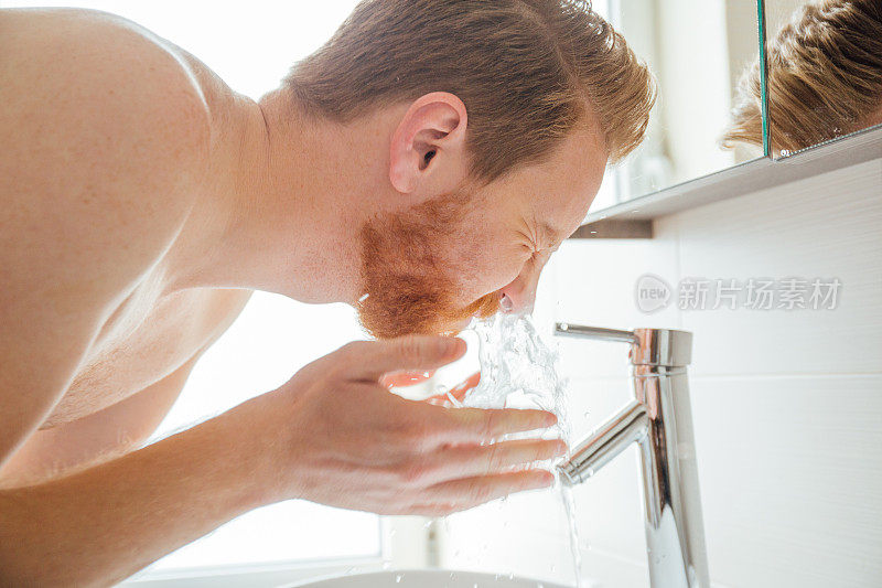 年轻英俊的男子在浴室的水槽上洗脸