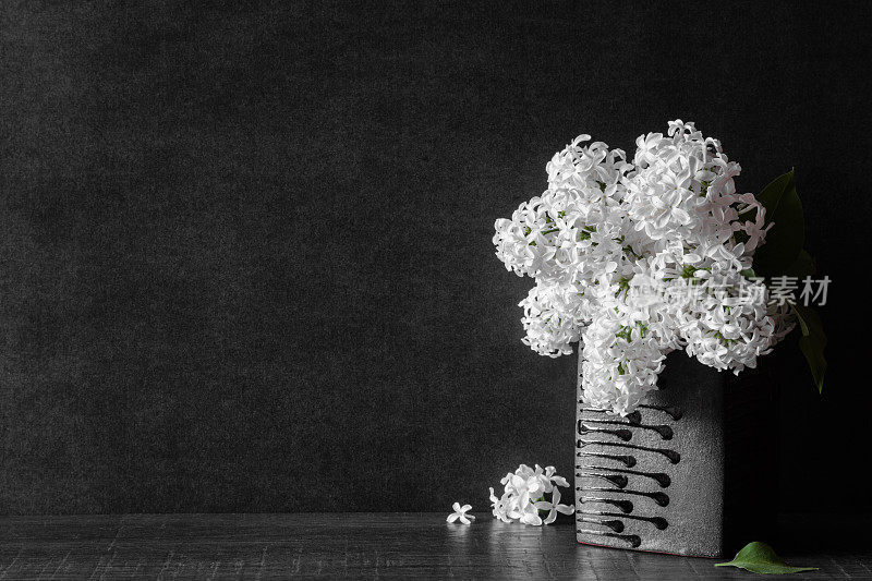 新鲜的白色丁香花束在黑色花瓶与落花在黑暗的背景。慰问卡片。空的地方，情绪化的文字，引用或语录。前视图。
