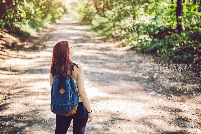 女旅行者背着背包走在森林里的小路上。