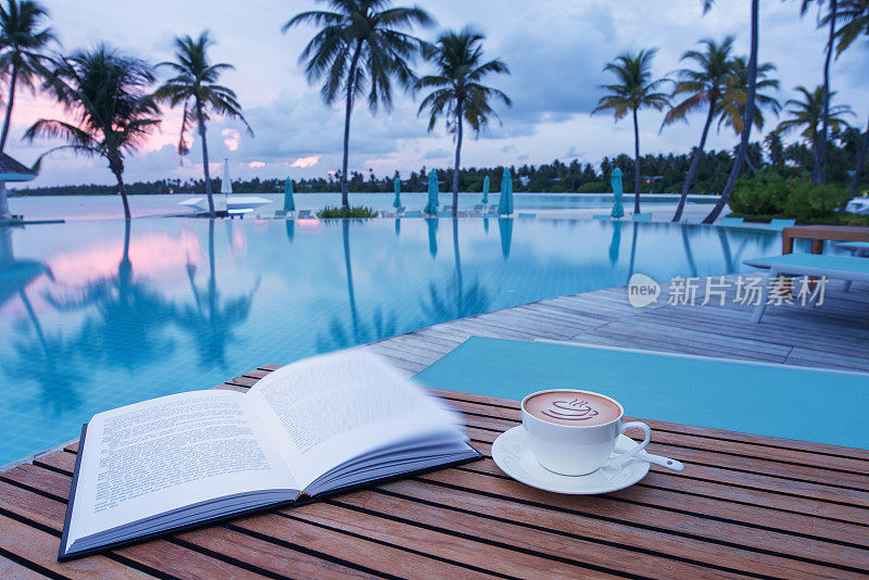 日落时分，在游泳池旁边的木桌上放上一杯咖啡和一本书