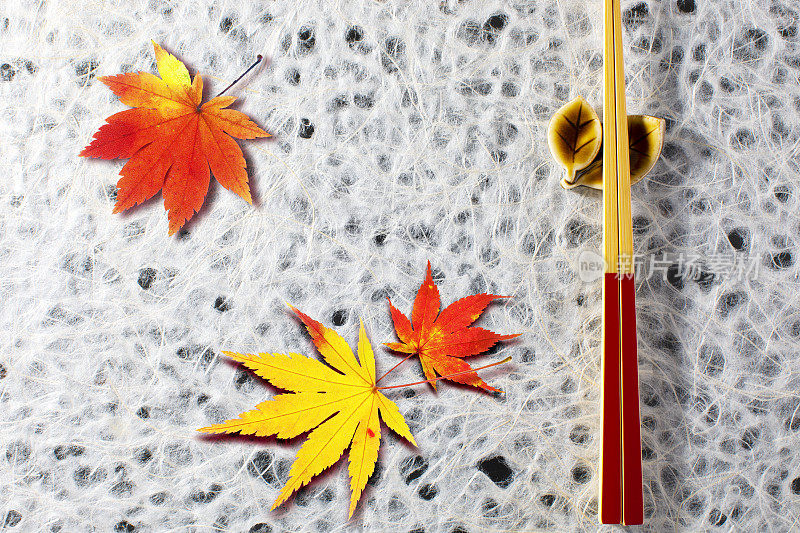 日本枫树和山葵的秋天。角度为鸟瞰图，背景为白色日本纸，放置筷子和筷子架，并有边缘。