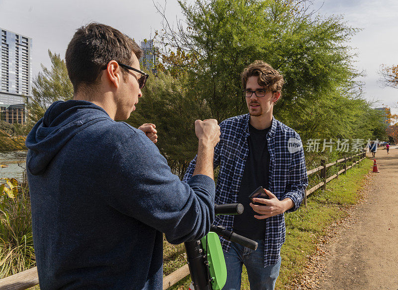 两个租来的电动摩托车的年轻男性朋友在公园里聊天