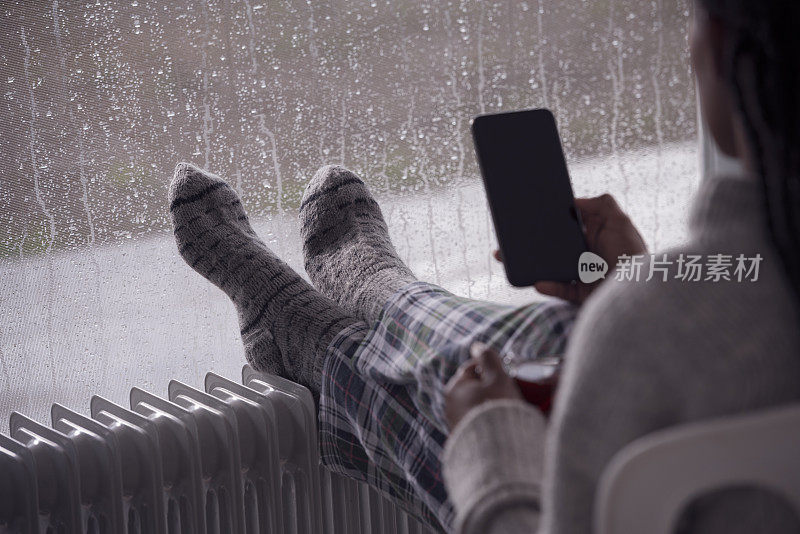 一位女士在电暖器前用智能手机加热腿。