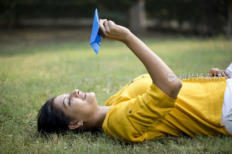 一个快乐的女人躺在公园的草地上扔纸飞机