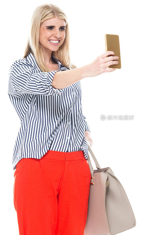 白种人年轻女性站在白色背景前，穿着漂亮的休闲装，拿着钱包，用手机拍照