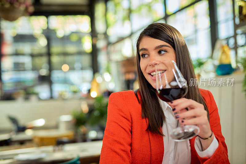 微笑的白人优雅的女商人坐在餐厅，拿着一杯葡萄酒，享受午餐。