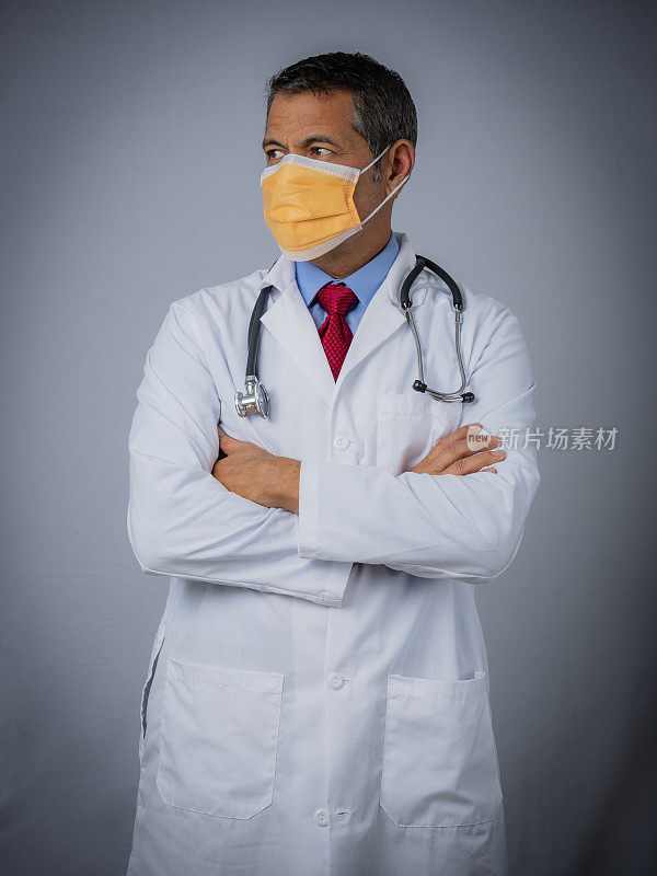 一个医生的肖像，看着他的右边，交叉双臂，戴着外科口罩
