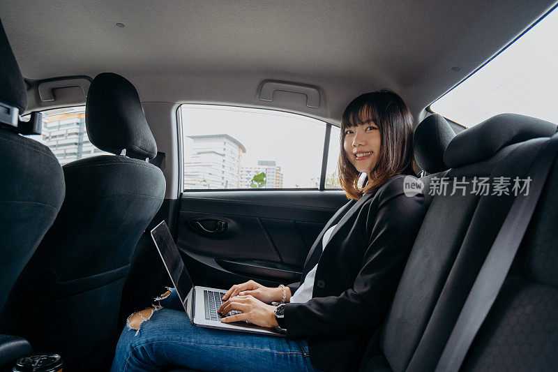 年轻的亚洲女商人在出租车上使用笔记本电脑