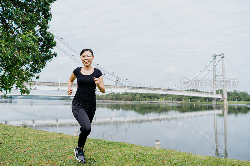 运动的亚洲华人妇女在湖花园跑步在早上