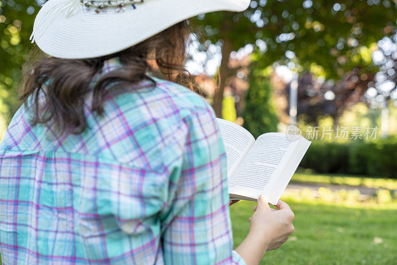 一位可爱的年轻女子在美丽的公园里悠闲地读着一本引人入胜的小说