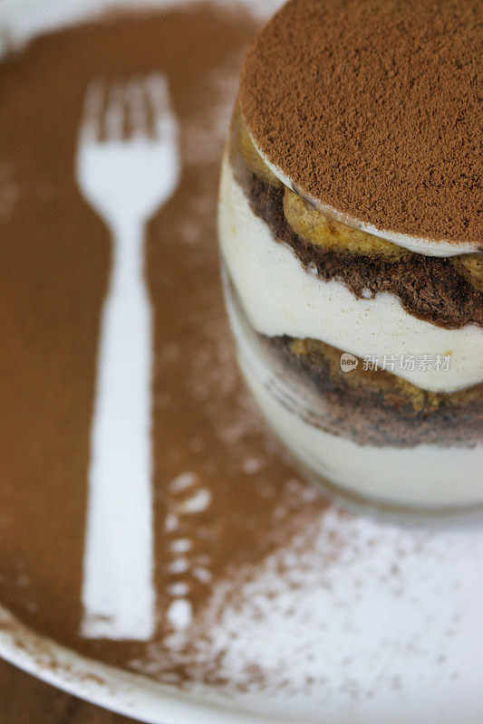 这是一个意大利餐厅自制的咖啡提拉米苏甜点，放在一个小玻璃盘子里，上面有马斯卡邦奶油、巧克力和海绵蛋糕，这是一个撒着可可粉的浓咖啡布丁