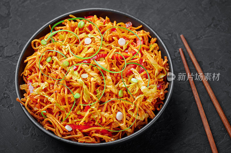 在黑色的石板桌面上，黑色碗里的中国贝勒。中国的巴勒是印中美食，以油炸客家面、蔬菜和四川酱为特色的街头小吃