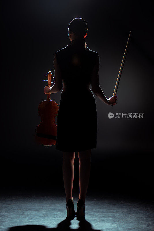 黑暗的舞台上，女音乐家拿着小提琴的剪影