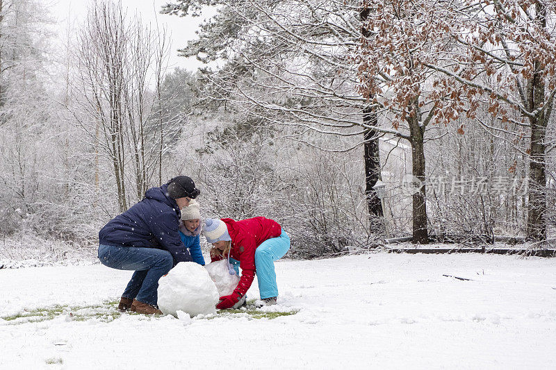 一个白人家庭和一个孩子正在堆雪人。妈妈，爸爸和女儿都五岁了。