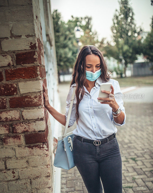 戴着面具的女孩在街上看手机