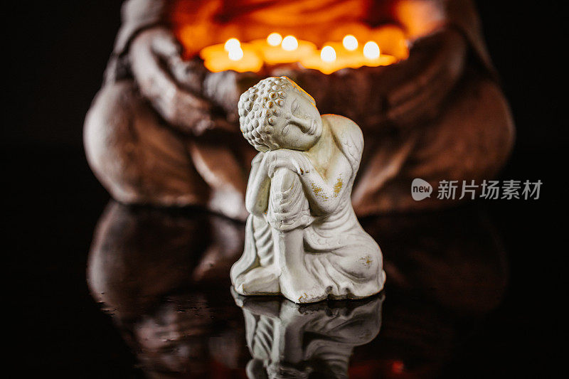 慈悲佛像与倒影在另一个佛像前，举着点燃的蜡烛