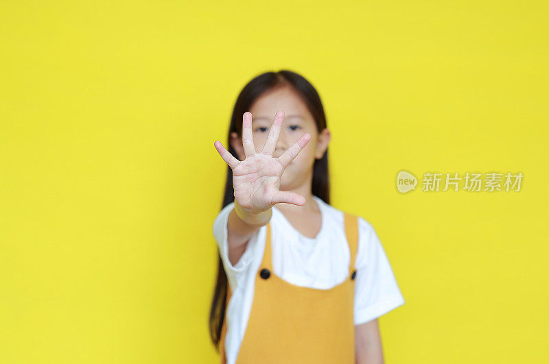 亚洲小女孩手心在黄色背景上做停车标志。否定和严肃的手势概念。选择手边的焦点