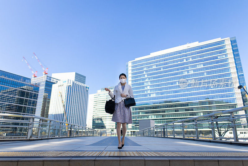 年轻的女商人戴着防护面罩走在城市的人行道上