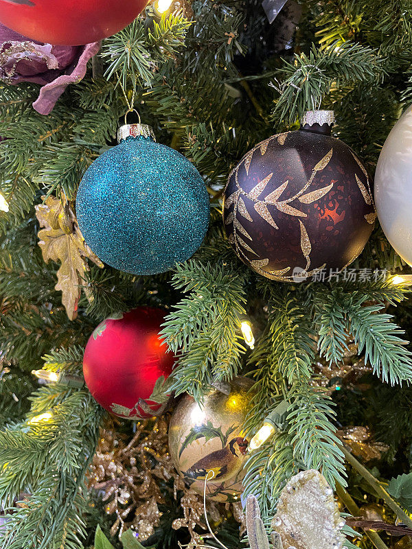 图像的蓝色闪光，红色，紫色和金色闪光图案的小玩意挂在人造圣诞树树枝的线，云杉针，模糊的白色精灵灯的背景