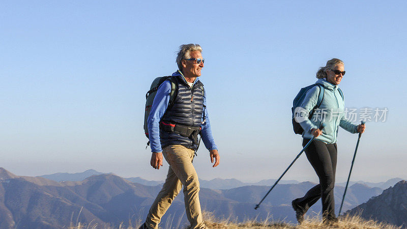 成年夫妇沿着长满青草的山脊徒步旅行