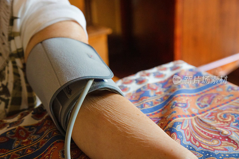 一位老年妇女在家中用监控设备测量血压时，胳膊上的特写镜头